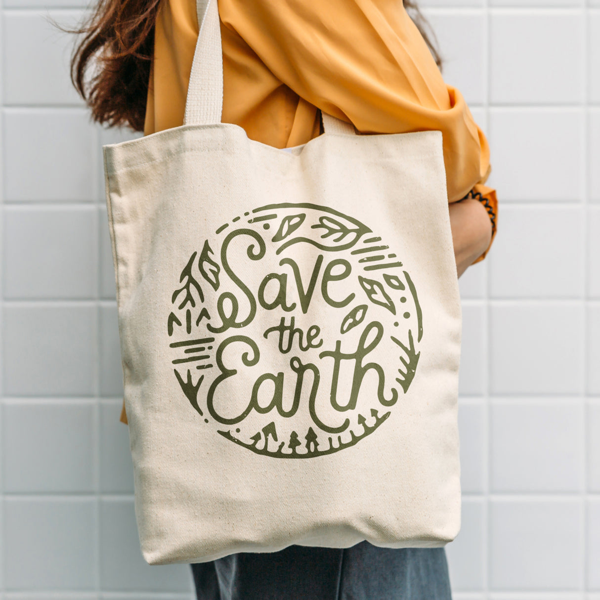 Person holding a tote bag with 'Save the Earth' design against a tiled wall printer with ricoma dtf 2402